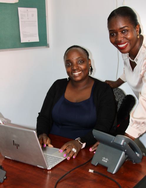 AYF member Doreen K. Serunjogi, is seated in her role as UCU Assistant Registrar on the Mukono campus, with Mbone Brenda, an international work study student from Kenya.