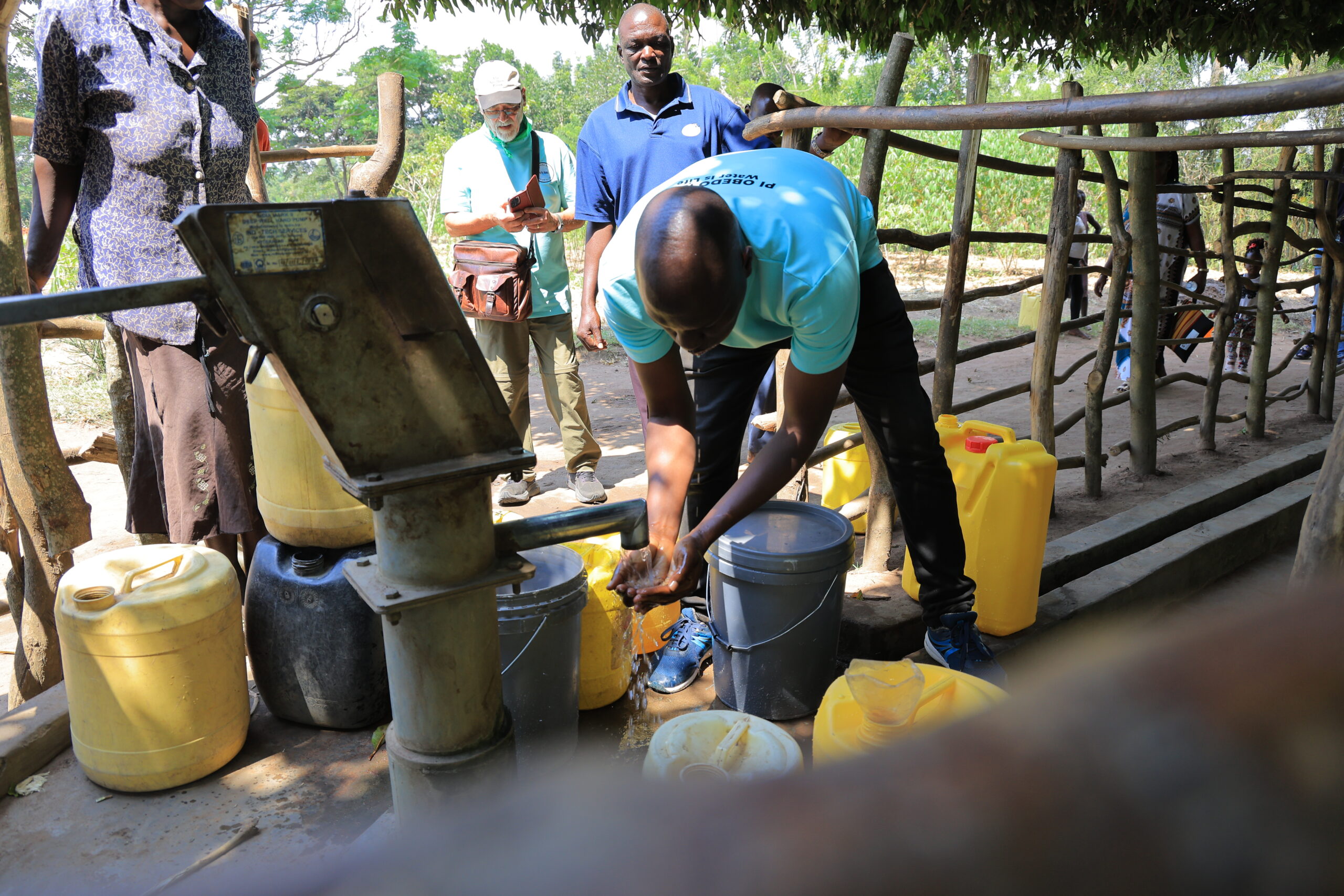 Frank Obonyo tastes water at one of three borehole projects he has led within his native village. Making notes on his phone in background is Ohio resident Mike Holm, one of the Americans who helped fund the clean water under Frank’s leadership.